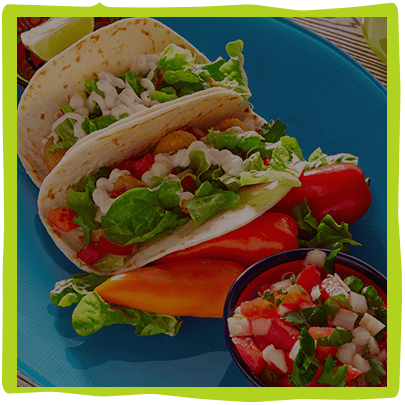 Two soft fish tacos on a blue plate with salsa and peppers